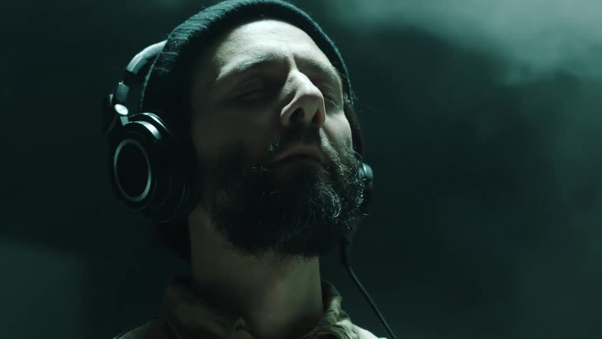 A man wearing headphones with eyes closed nods his head to music while smoke hangs in the air behind him
