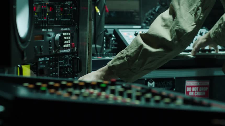 A man is pressing buttons and dials on the music equipment