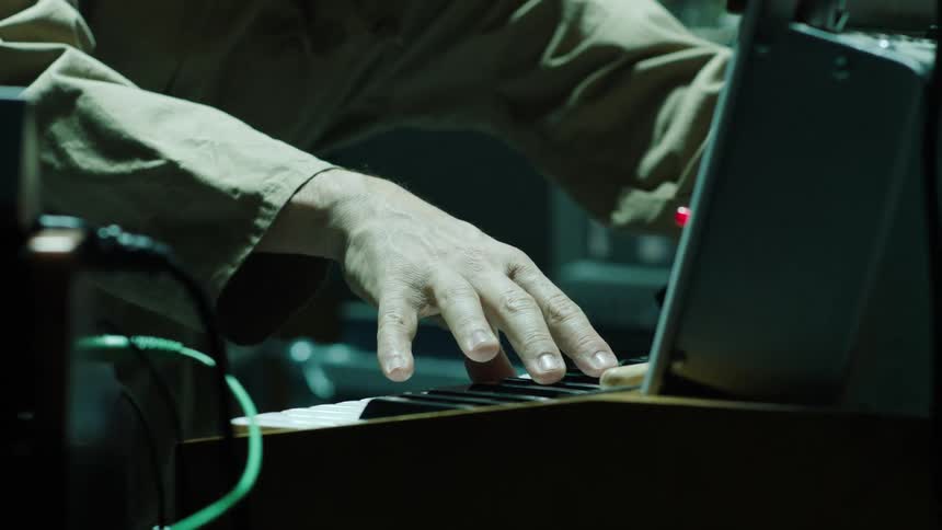 Musician surrounded by electronic equipment uses a keyboard