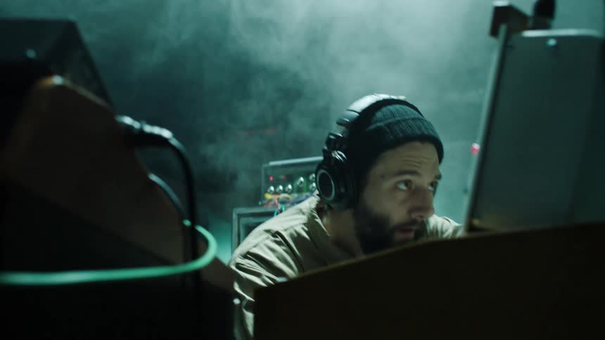 A man alternating between kneeling and standing while operating audio equipment in a dark smoky room