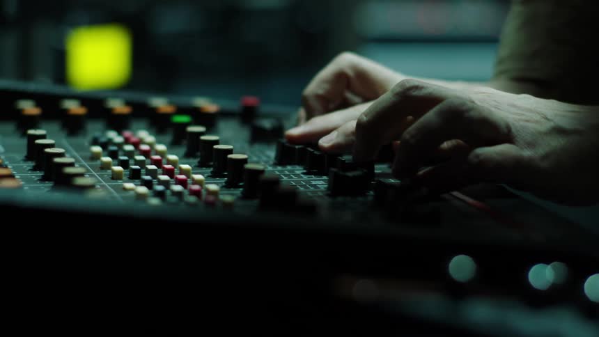 Man adjusts sliders and dials on sound mixing board
