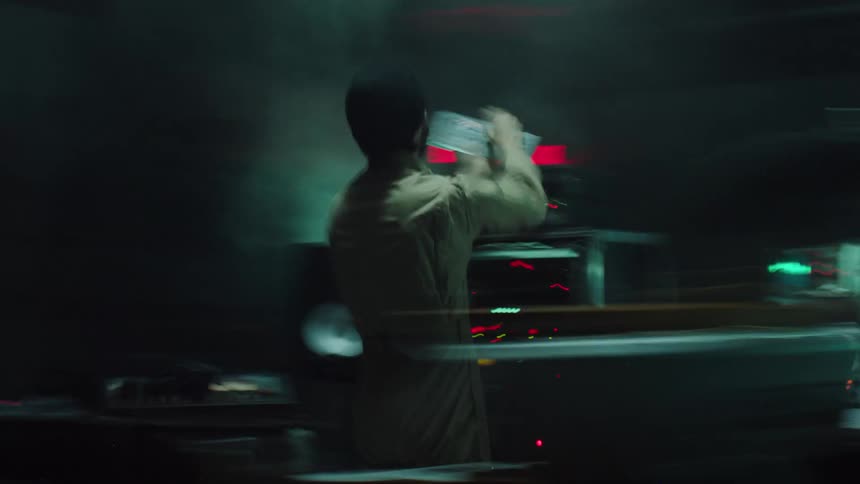 Dj moves among music equipment in foggy dark area