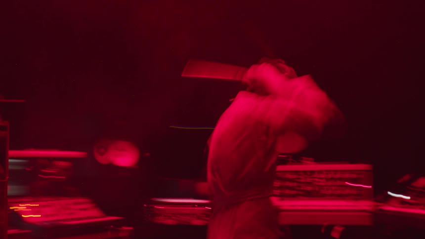A person frantically smashes equipment on desks in a red lit room