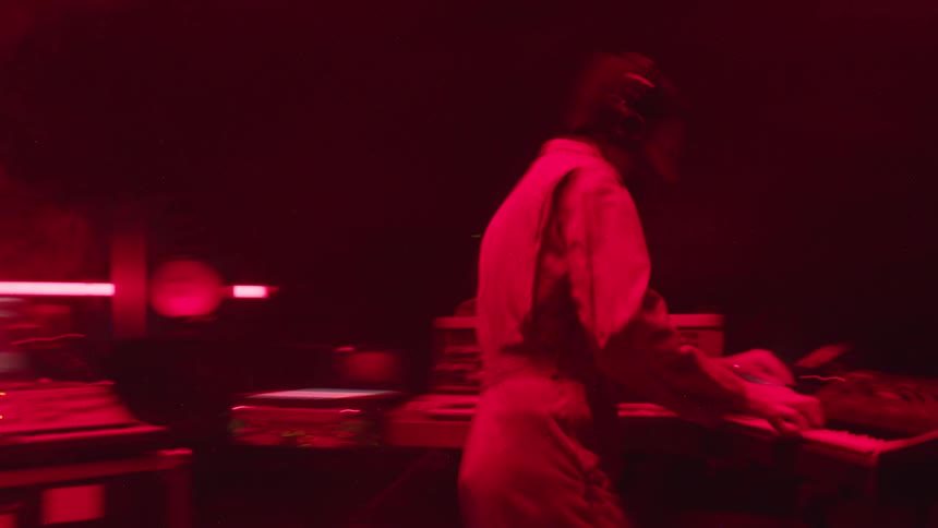 Man works on computer and other music equipment in red tinted room