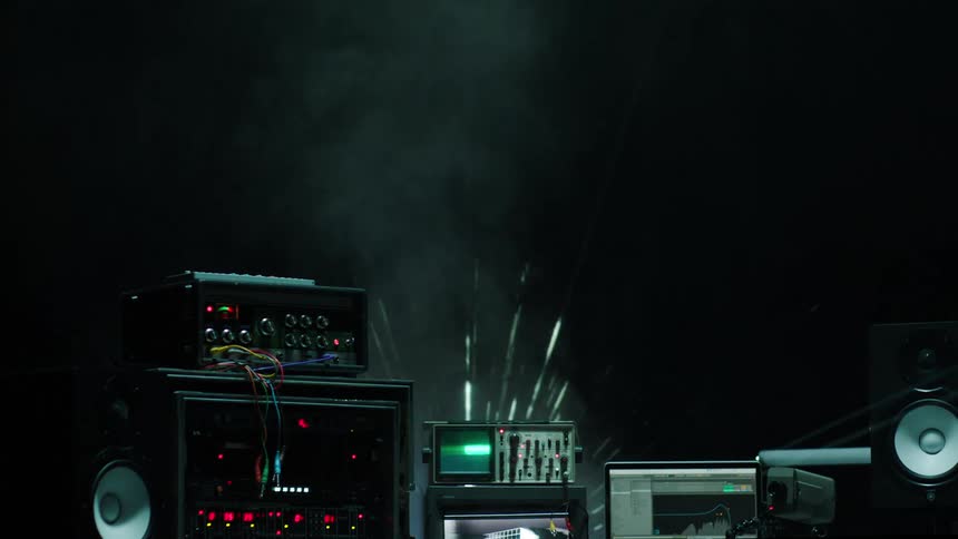 Powered on audio equipment in a dark room in front of smoke that has images being projected onto it