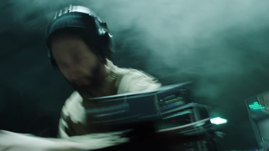 A man with headphones djing with equipment in front and behind him