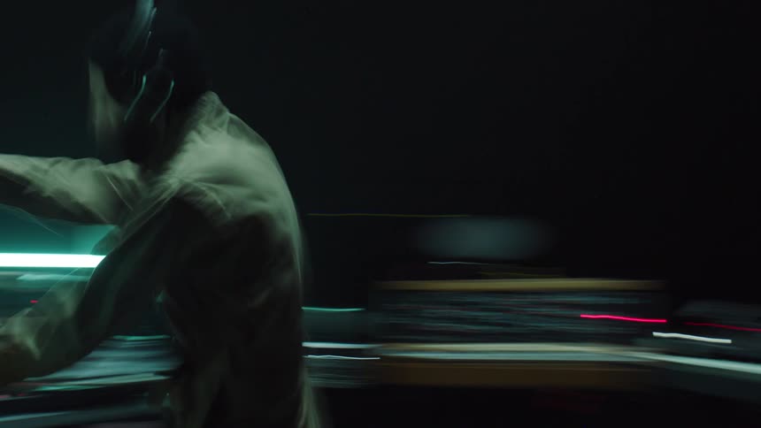 A man wearing coveralls and a headset moves from one piece of equipment to another as lights glow and everything spins and blurs