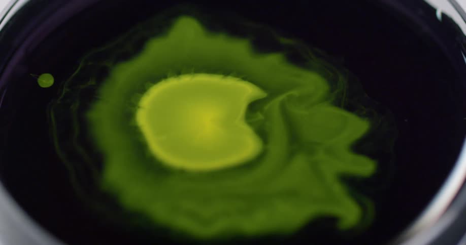 Paint drips into liquid in a bowl creating waves and patterns