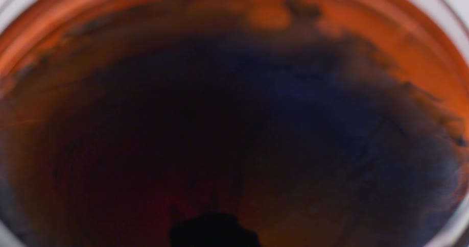 Drop of black dye falls on orange liquid