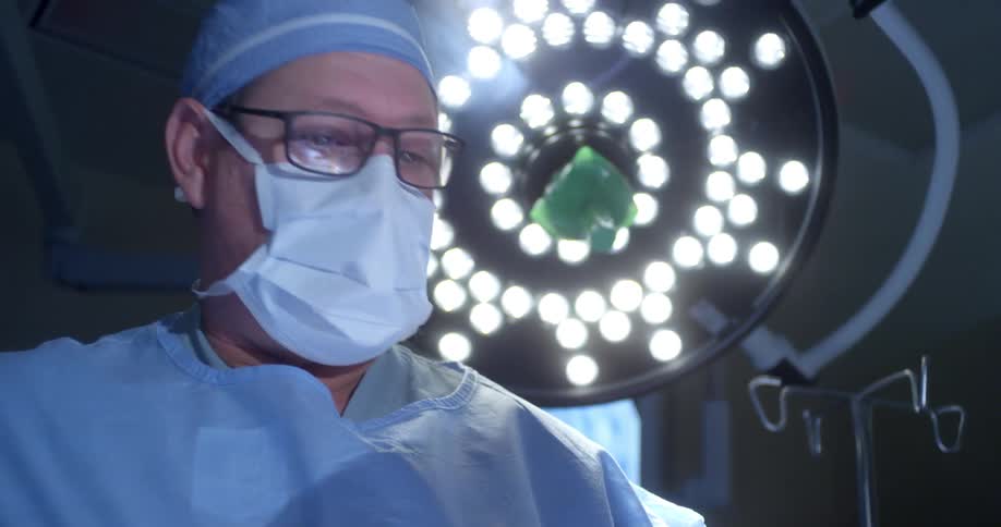 A surgeon wearing a mask and scrubs stands in an operating room