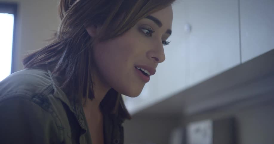 A woman in a room talking to someone with cabinets and windows in the background