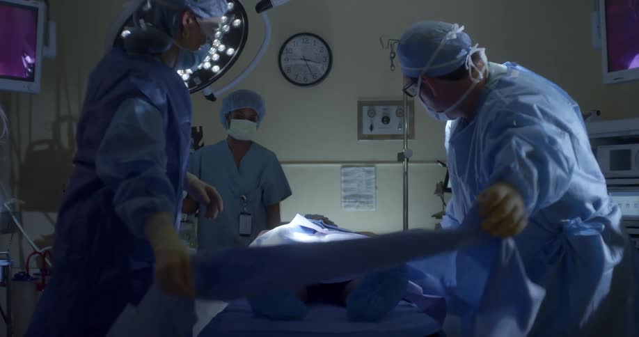 A surgeon and a nurse cover a patient with a blue blanket in an operating room