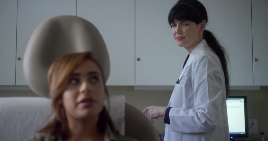 Female dentist with a white doctor coat talks to the patient sitting in a chair in a clinic