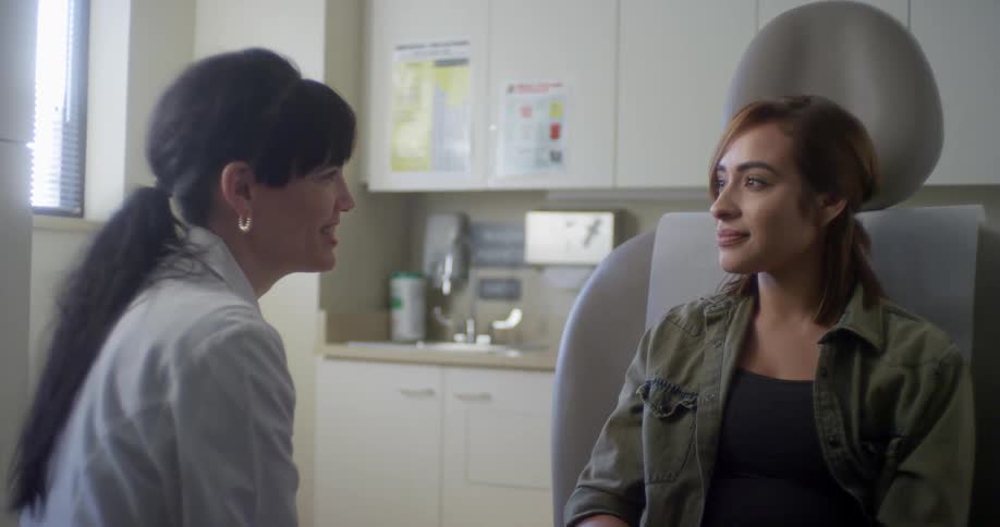 Woman in a lab coat talks to another woman sitting in a dentists chair