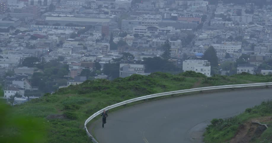 A blonde female jogger runs on a road near a large city neighborhood