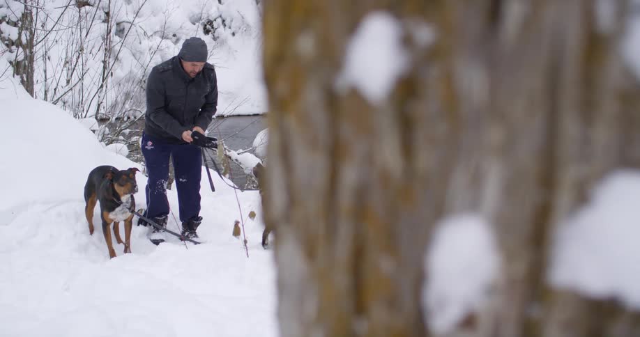 A white man stands in the snow with two dogs on leashes