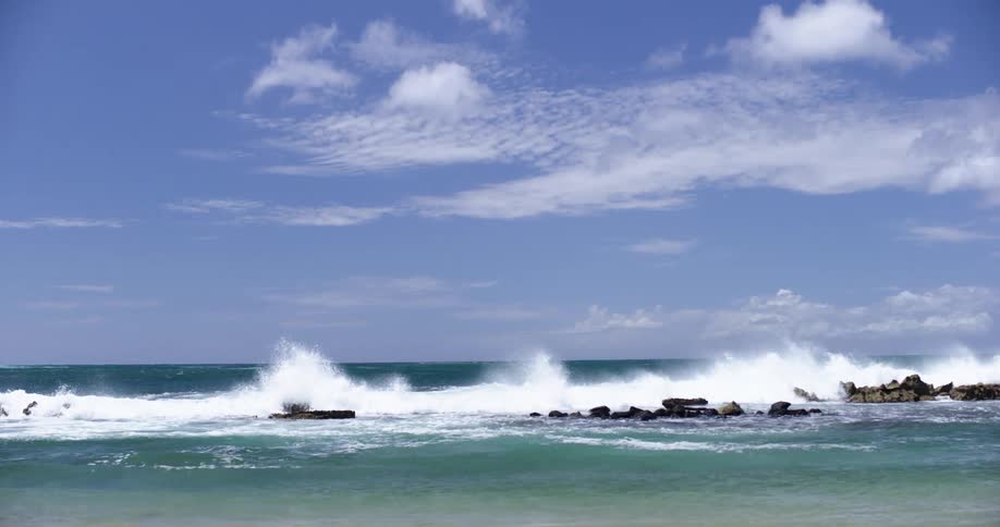 Ocean waves splash and crash against the rocks on a bright blue sky day