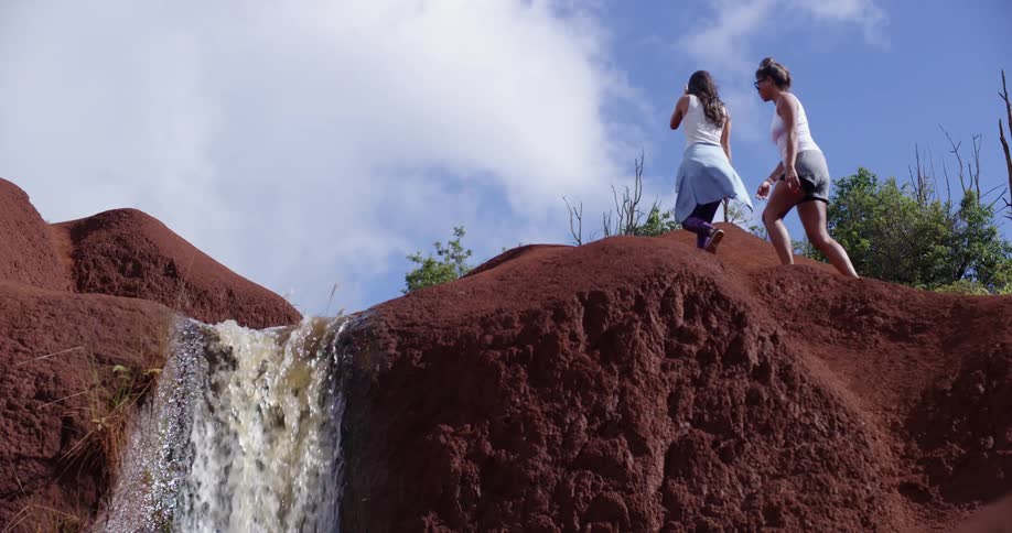 Two women hike up a cliff past a waterfall