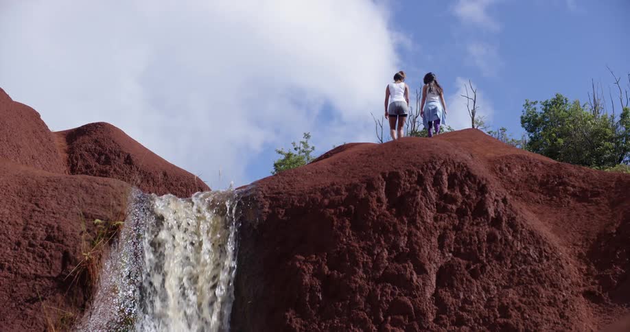 Two women walk on the top of hill next to a small waterfall