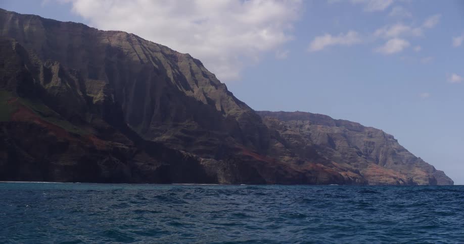 Waves roll near mountainous shoreline under slightlycloudy sky