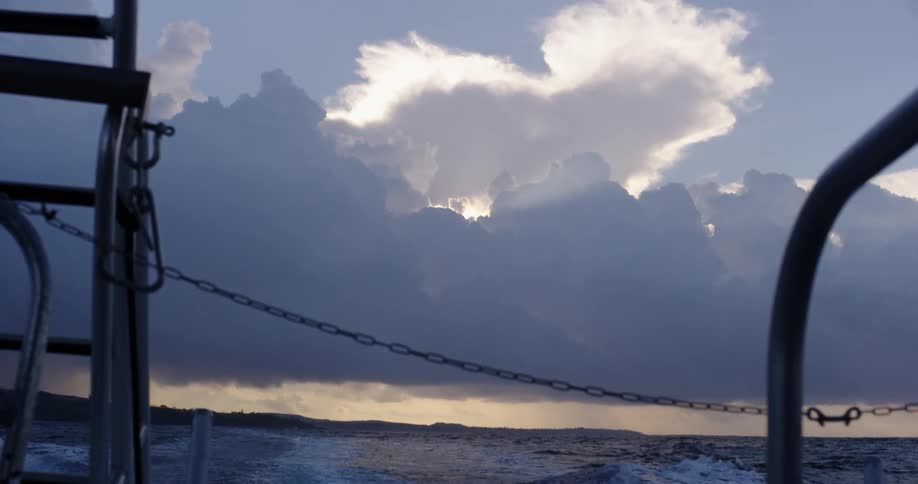 A boat churns through water as a rain storm hovers over the horizon