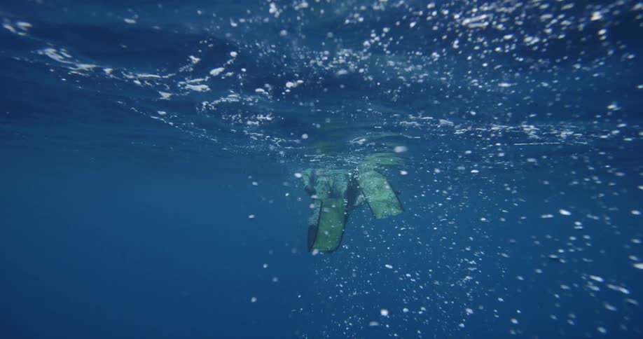Person wearing slippers leisurely swims underwater near surface