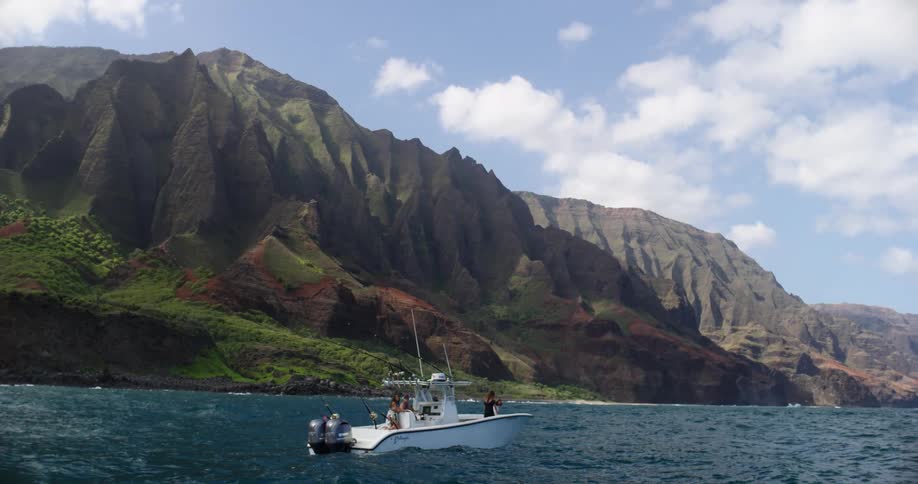 A boat with people on it floats in the water off of a coast dominated by a mountain range