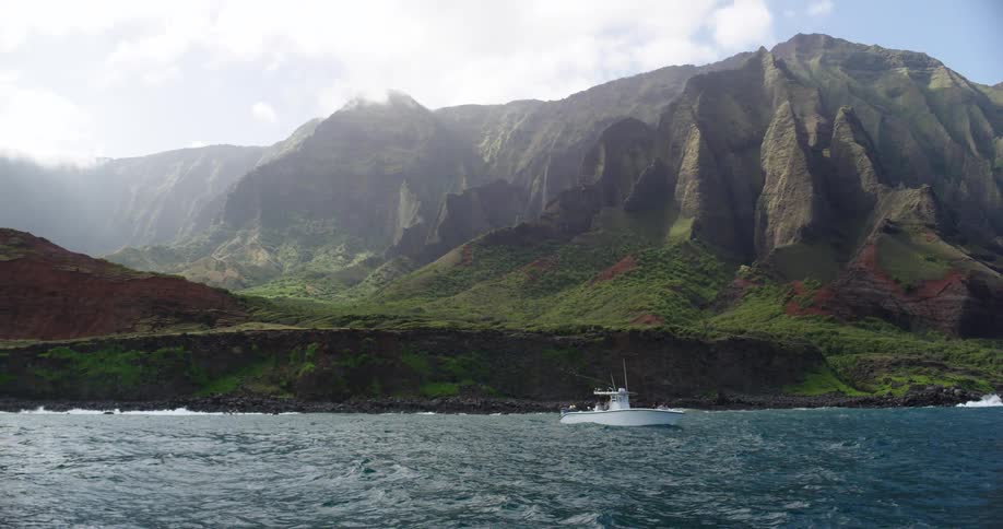 A small boat with passengers floats near the coast with a large rocky mountain in the background
