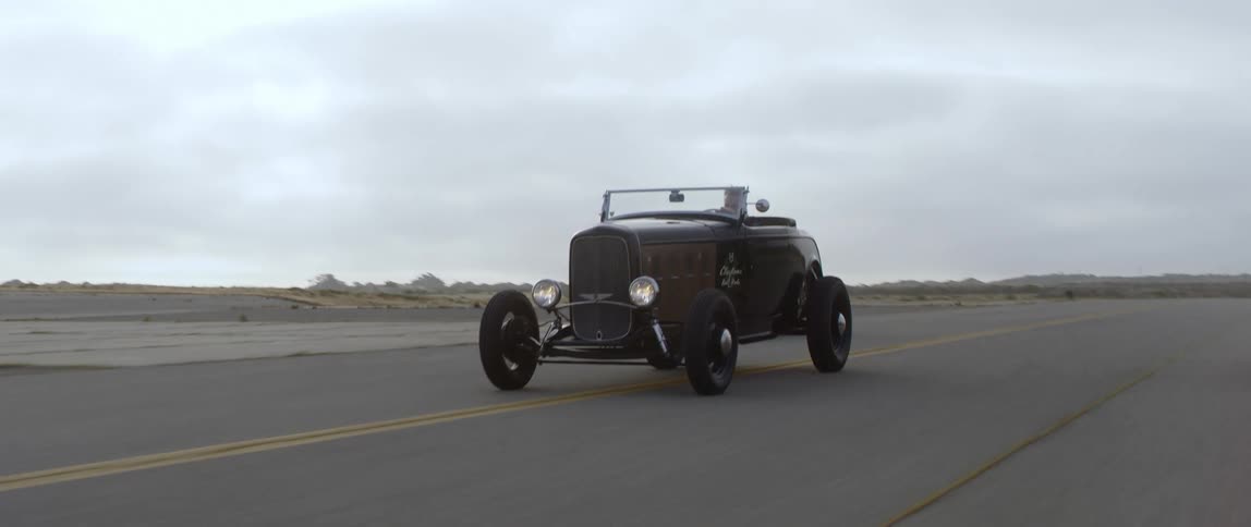 Men driving three classic cars on the road with the sky in the background