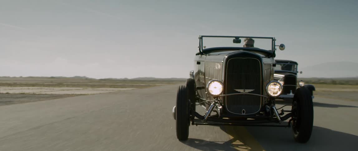 Three classic cars weave as they drive down a rural road