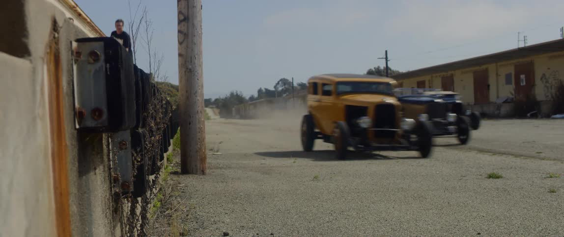 Two teens skateboard alongside three racing cars