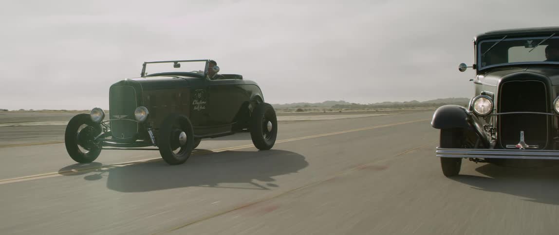 Three vintage automobiles race down the highway