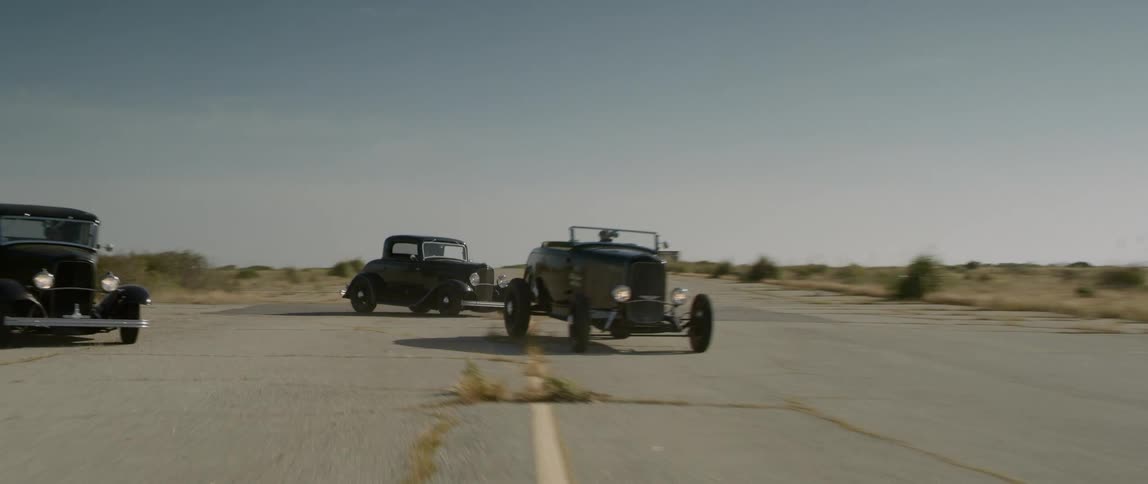 Three vintage cars race down a road