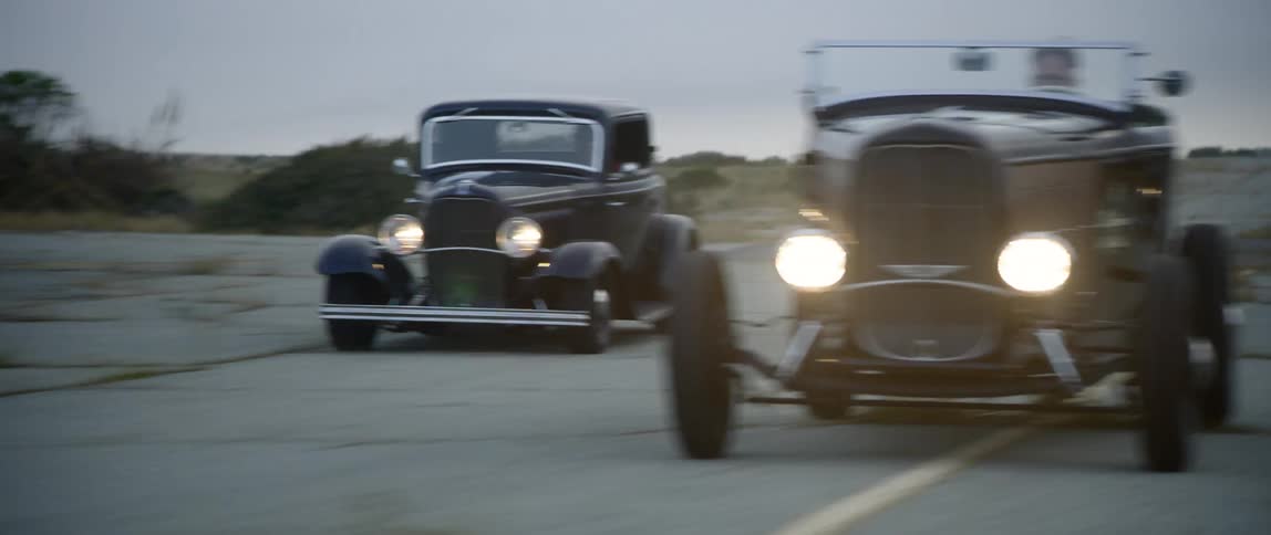 Three vintage cars are racing side by side