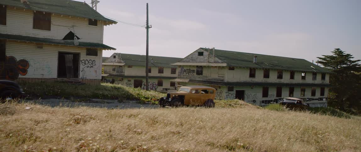 Three classic cars drive by a poor neighborhood