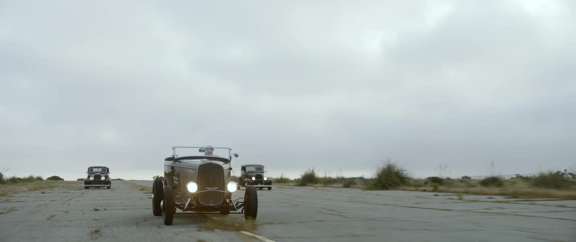Three classic cars race each other on a rural road