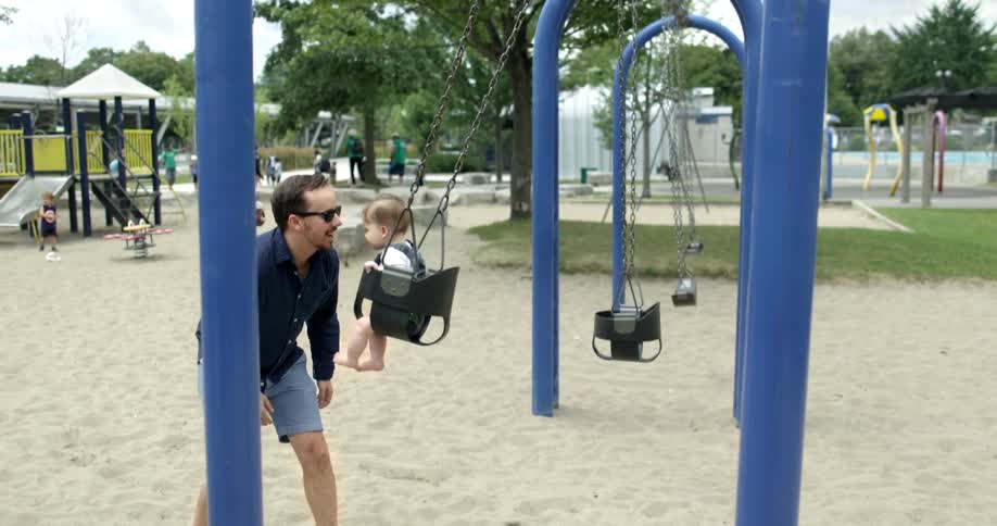 A young father pushes his toddler daughter on a swing at a playground