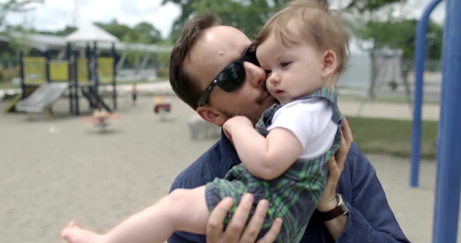 Father carries son and kisses him in the cheek in a playground