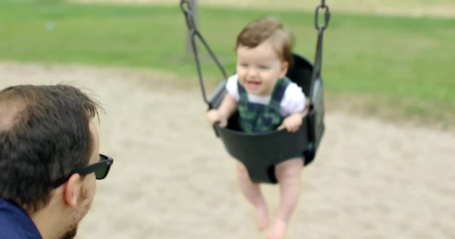 Father pushes his laughing son on swing set at park