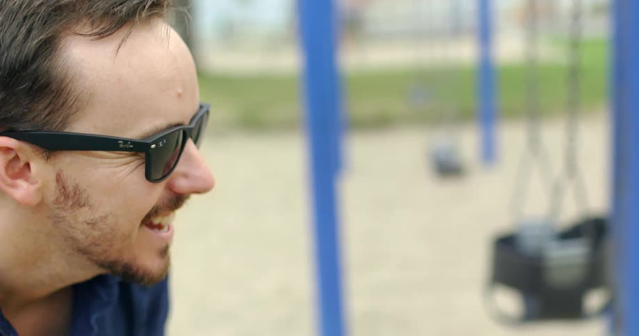 A dad makes faces as his baby swings towards him on the playground and both laugh and smile