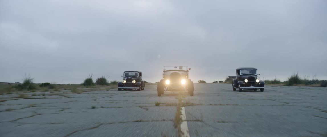 Three vintage cars racing down a street