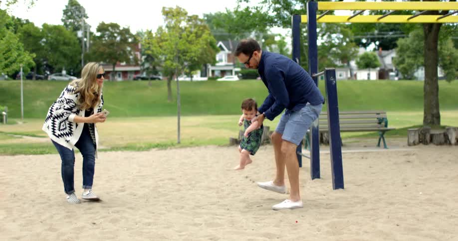 A mother and father play with their child at a playground in a park