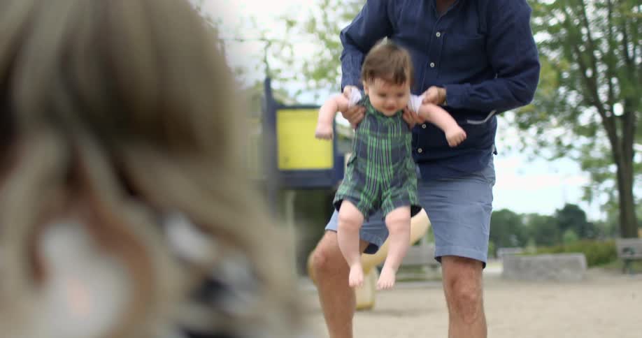 Father plays with toddler on a playground outdoors while mother watches