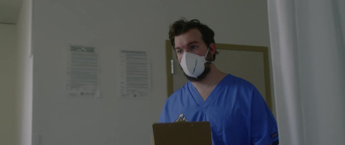 A doctor carrying a clip board walks in to a patient room