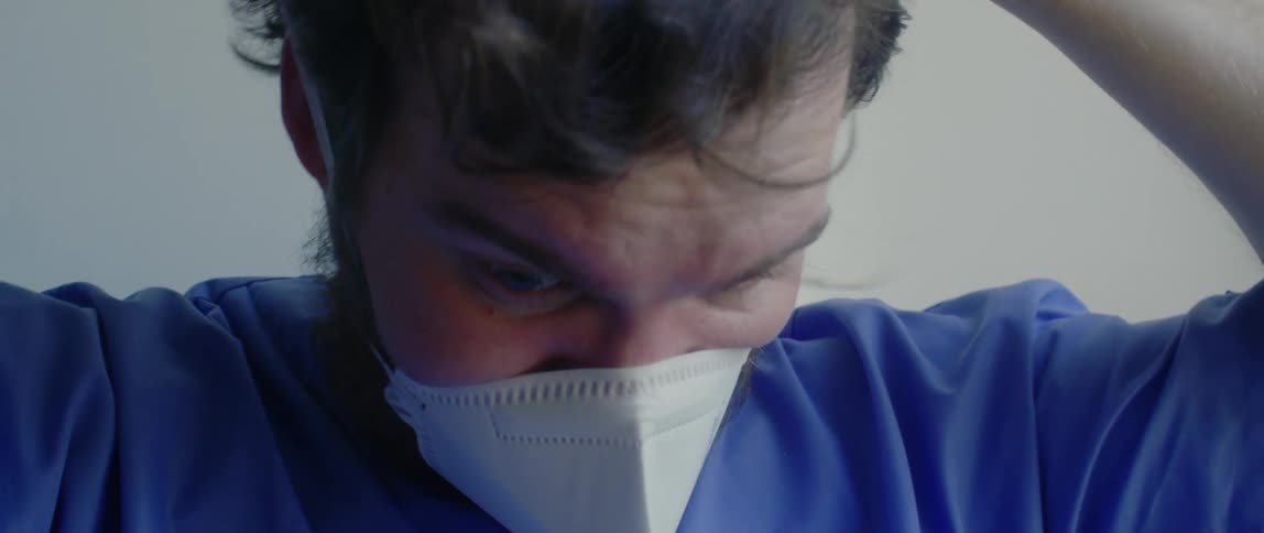 Bearded male nurse wearing blue scrubs puts on face mask