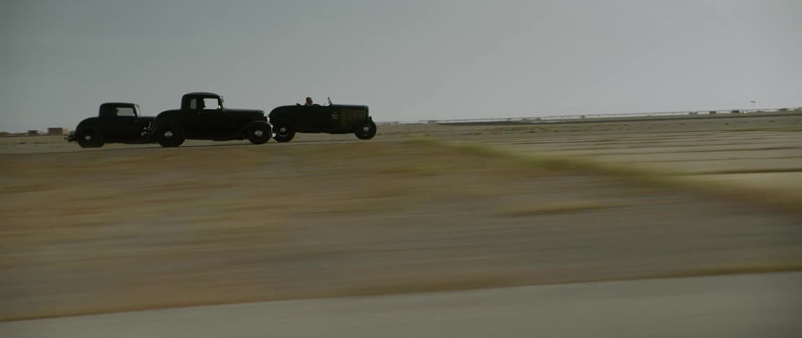 Three vintage cars race across area between grass lots