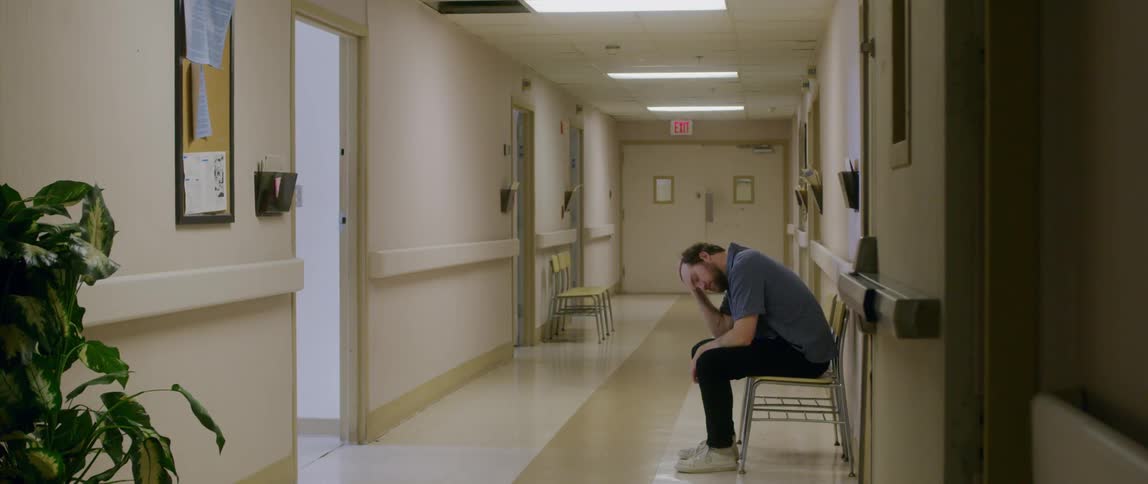 A doctor walks away from a worried man waiting in the hospital hallway