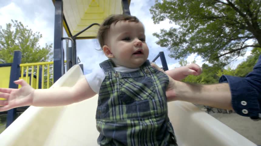A man helping a baby to slowly descend a slide on an outdoor playground