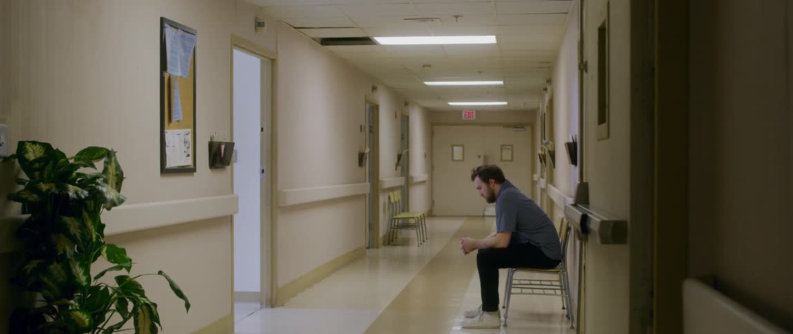 Man sits down on a chair in a hospital hallway to wait