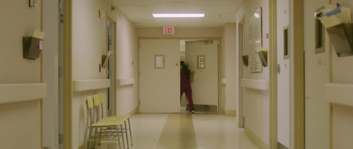 Nurse dressed in maroon walks through wide doors at end of hospital corridor